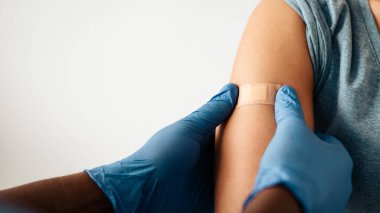 Hastanedeki hastalara kovid 19 salgınına karşı aşı. Koruyucu eldivenli Afrikalı Amerikalı doktorun elleri klinikteki hastalara yara bandı yapıştırıyor, kapatıyor, boş yer açıyor, kırpılıyor.