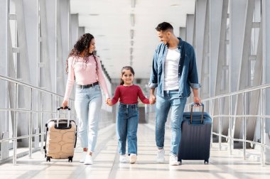 Birlikte seyahat ediyoruz. Havalimanı Terminali 'nde bavullarla gezen neşeli bir Arap ailesi, Mutlu Orta Doğulu ebeveynler ve uçuş kapısına giderken bavullarını taşıyan kadın çocuk,