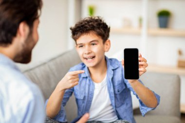 Bana bak. Mutlu çocuk, babaya boş siyah ekranlı akıllı telefonu gösteriyor ve onu gösteriyor, maket için uygun bir yer. Modern teknolojiler, yeni uygulama kavramı