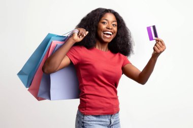 Nakit Kavramı. Kredi kartıyla mutlu siyah kadın pozları ve beyaz arka planda alışveriş torbaları, neşeli Afrikalı Amerikalı kadın büyük indirimlerden zevk alıyor ve satın alma teklifleri, Panorama, Kopya Boşluğu