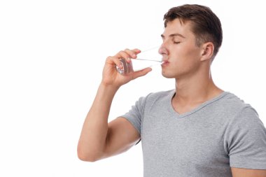 Yakışıklı, kaslı, beyaz arka planda, panoramada, kopyalama alanında izole edilmiş camdan su içen beyaz tenli genç bir adam. Covid-19 salgını sırasında sağlık hizmeti, su dengesi ve su kaybı, stüdyo çekimi