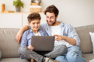 Babasının oğluna dizüstü bilgisayar kullanmayı ya da interneti birlikte gezmeyi öğretmesi oturma odasında rahat bir koltukta oturup evde boş zaman geçirmesi. Modern teknolojiler ve ebeveynlik kavramı.