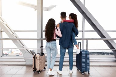 Uçaktan inerken pencereden dışarı bakan üç kişilik bir aile, ebeveynler ve küçük kızı, uçuşlarını beklerken manzaranın keyfini çıkarıyorlar, bavullarıyla birlikte tersanede dikiliyorlar.