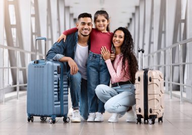 Arap anne, baba ve küçük kızı, uçuştan önce havaalanında poz veriyorlar, üç kişilik mutlu bir ortadoğu ailesi, birlikte tatile çıkmaya hazırlanıyorlar,