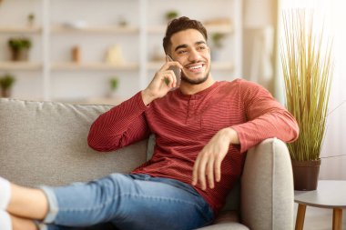 Sıcak oturma odasındaki kanepede uzanan yakışıklı orta doğulu adam sevgilisiyle ya da arkadaşıyla cep telefonuyla konuşuyor. Gülümsüyor ve pencereden bakıyor. Evinin içini kopyalıyor.