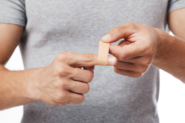 Мускулистый кавказский мужчина тысячелетия, страдающий от боли в пальце и накладывающий пластырь, изолированный на белом фоне, копирующий пространство, крупным планом. Парень чувствовал боль, помогал себе с травмой, обрезал