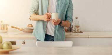 Evde rahatla. Genç tanınmayan bir adam mutfakta sabah kahvesini içiyor, elinde sıcak bir bardakla hayal kuruyor, başka yere bakıyor, ev içi istirahatinin keyfini çıkarıyor, boş bir mekanla manzaranın keyfini çıkarıyor.