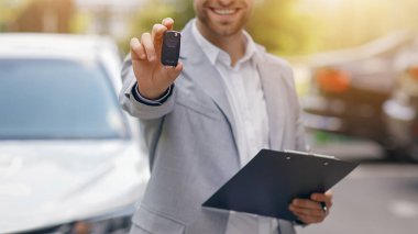 Acente satışları, dağıtımcı bakım salonundan yeni bir araba almayı teklif ediyor. Gülümseyen yakışıklı adam takım elbiseli satıcı yeni beyaz araba, açık hava, seçici odak, serbest alan sahibi için anahtar veriyor.