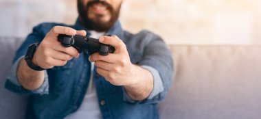 Hafta sonu tatili. joystick kullanan, online video oyunları oynayan, oturma odasındaki koltukta oturan, seçici odaklı neşeli bir Arap. Mutlu genç adam evde boş zaman geçiriyor.