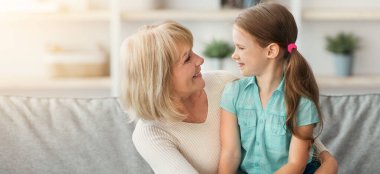 Birlikte boş zaman geçirmek. Gülümseyen olgun bir kadın ve anaokulu çocuğunun portresi. Oturma odasındaki kanepede güzel bir sohbet ediyorlar. Torunum büyükannenin kucağında oturuyor.
