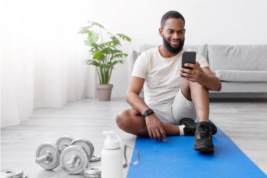 Gülümseyen bin yıllık Afro-Amerikan sakallı halı, halterler ve akıllı telefonlara bakan bir şişe suyla odanın içinde yerde oturuyor. Ev işi, ekipman, sağlık ve araç gereçle birlikte vücut bakımı