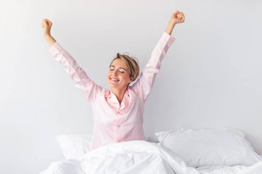 Sıradan Sabah Vakti. Pembe pijamalı neşeli kadın uyandıktan sonra kollarını açıyor, mutlu kadın battaniyenin altında gözleri kapalı ve beyaz çarşaflar altında oturuyor.
