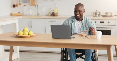 Sağlık hizmeti, düzgün beslenme ve evde iyi bir kahvaltı. Gülümseyen Afro-Amerikalı tekerlekli sandalyede sakat kalmış laptopla yemek yiyen ve dizüstü bilgisayar izleyen biri.