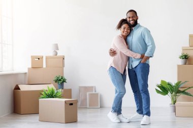 Gülümseyen Afro-Amerikan bir aile yeni bir dairede kucaklaşıyorlar. Odanın içinde kutular ve bitkiler var. Evli çift tadilattan zevk alıyor, daireye taşınıyor ya da ev alıyor.