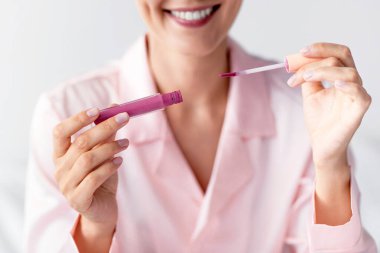 Pembe ruj kullanan, tanınmayan bir genç bayanın gülümseyiş görüntüsünü kapatın. Neşeli kadın elinde tüp ve fırça tutuyor, günlük makyaj yapıyor, kozmetik ürünler uyguluyor, dudak parlatıcısını destekliyor.