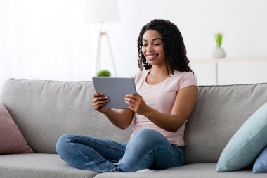 Sosyal ağlarda modern sohbet, online görüşme, iş ve evde video izleme, covid-19. Mutlu Milenyum Afro-Amerikan kadınları Tablet 'e bakın. Oturma odasında yakınlaştırma toplantısı yapın.