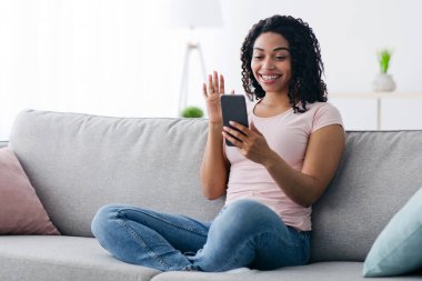 Çevrimiçi sohbet, boş zamanlarında evde zum toplantısı, yeni normal ve sosyal mesafeler, covid-19 salgını. Mutlu Milenyum Afro-Amerikan kadınları oturma odasında el sallıyor ve telefon ediyor.