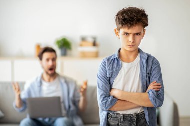 Karantina sırasındaki aile sorunları. Kızgın baba, evdeki kanepede dizüstü bilgisayarla otururken oğluna bağırıyor ve kolları bağlı çocuğa odaklanıyor. Nesiller yanlış anlama kavramı