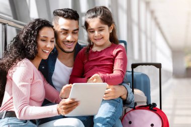 Havalimanında dijital tablet kullanan genç ve güzel bir orta doğu ailesi, mutlu Arap ebeveynler ve kadın çocuk bakımı haritası veya internet üzerinden otel rezervasyonu yapan, birlikte seyahat etmekten hoşlanan, yakın plan