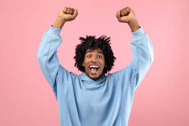 Muzaffer siyahi genç adam kollarını başının üstüne kaldırıyor pembe arka planda heyecanla bağırıyor. Başarı ya da başarıyı kutlayan Afro-Amerikan gençliği önemli bir hedefe ulaşır.