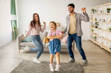 Eğlenceli aktiviteler. Coşkulu bir doğulu ailenin çocuğuyla birlikte taşınıp dans etmesi. Mutlu kız, baba ve anne eğleniyor, evde birlikte vakit geçiriyorlar.