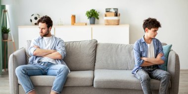 Aile nesli çatışması. Baba ve oğlu tartışmadan sonra birbirlerini görmezden gelerek koltuğun farklı taraflarında oturuyorlar. İnatçı baba ve çocuk çatışmadan sonra bakıp konuşmazlar.