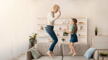 Sevimli küçük kız eğleniyor gülümseyen büyükannesi ile birlikte, Kanepeye atlama iskambil mutlu büyükanne ve kanepe, Büyükanne ve torunu evde oynarken gülüyor dans etkin çocuk torun