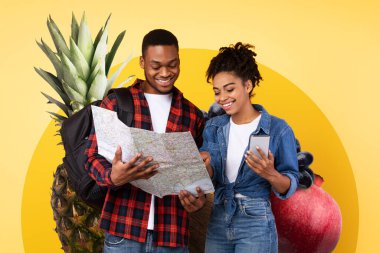 İki birey, renkli meyve gösterisiyle çevriliyken ayrıntılı bir haritayla meşgul oluyor. Sağlıklı besin seçeneklerini ve sundukları vitaminleri araştırmayı seviyorlar. Beslenme bilincini vurguluyorlar..