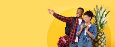 Açık sarı arka plan, Afro-Amerikan çiftin seyahat ederken eğlendiği meyvelerden oluşan bir kolajı tamamlıyor. Sağlıklı beslenme, kopyalama alanı, panorama