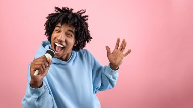 Rock yıldızı. Havalı siyahi bir gencin portresi şarkı söylüyor, mikrofon kullanıyor, pembe stüdyo arka planında karaoke yapıyor. Kaygısız Afrikalı Amerikalı ergen şarkıcı canlı müzik konseri veriyor.