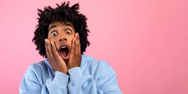 Havalı siyahi genç adam yüzüne dokunuyor, pembe stüdyo arka planında dehşet içinde bağırıyor. Afro-Amerikan ergen duyguları şok edici ya da korkmuş, korkunun duygularını ifade ediyor.