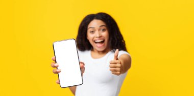 Baş parmak jesti. Aşırı neşeli Afro-Amerikan bayan işaret gibi görünüyor, sarı arka planda kameraya gülümsüyor, stüdyo çekimi, boş alanı olan bir panorama. Beyaz tişörtlü kadın bir şeyi onaylıyor.