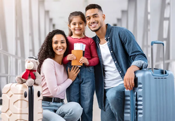 Havalimanı terminalinde üç poz veren mutlu orta doğulu aile, neşeli Arap ebeveynler ve küçük şirin kızlarının bavulları, pasaportları, biletleri ve kameralara gülümseyen, seyahat etmeye hazır.