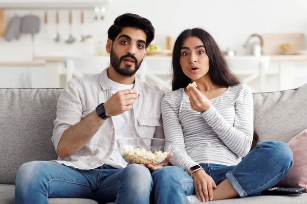 Evdeki korkutucu, ilginç ve heyecan verici sinema ve insani duyguların ifadesi. Şaşırmış genç Arap kadın ve erkek ağızları açık ve patlamış mısırlı oturma odasında televizyon seyrediyor, boşluğu kopyalıyor.