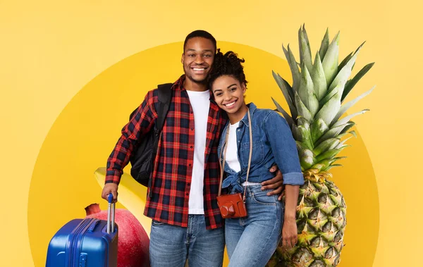 Neşeli bir çift, parlak sarı bir arka planda taze meyvelerin olduğu bir arkaplanda yan yana durur. Bavul taşıyorlar ve gülümsüyorlar. Eğlenceli, sağlık bilincine sahip bir seyahat havası yaratıyorlar..