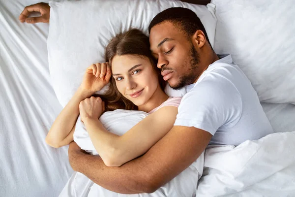 Genç siyahi adam uyuyor ve beyaz güzel kız arkadaşına sarılıyor. Şefkatli, çok ırklı bir çiftin sabahları birbirlerine sarılıp...