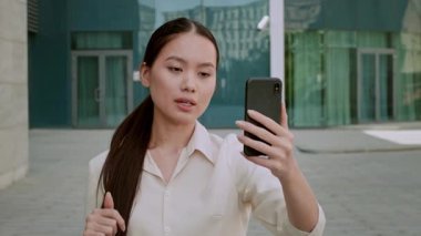 Modern bir şehir ortamında açık havada duran bin yıllık bir kadın aktif olarak sanal bir toplantıya katılıyor. Meslektaşlarıyla iletişim kurarken odaklanmış ve kendinden emin görünüyor..