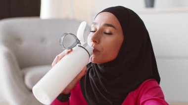 Genç Müslüman bir kadın evinde çalışmaya ara veriyor. Şişeden su içiyor. Spor kıyafetleri giyiyor ve tesettür takıyor. Sağlıklı bir yaşam tarzını destekliyor..