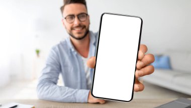 Çevrimiçi reklam. Gülümseyen Genç Adam Evde Masada otururken Büyük Boş Ekran ile Akıllı Telefon Gösteriyor, Yakışıklı Milenyum Adamı Yeni Mobil Uygulama ya da Web Sitesi, Kolaj,