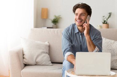 Başarılı iş konuşmaları. Cep telefonunda konuşan bir adam dizüstü bilgisayarını kullanıyor. Kapalı koltukta oturuyor. Boşluğu Kopyala