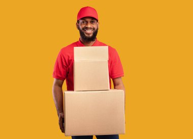 Ekspres teslimat. Siyah Kurye, elinde karton kutular ve paketler tutuyordu. Sarı Stüdyo Arkaplanda duruyordu. Çevrimiçi mağazadan mal getiriyordu..