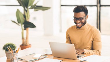 Başarılı bir Freelancer. Gülümseyen ve ofisteki bilgisayarda çalışan mutlu afro adam. Kopyalama alanı, panorama