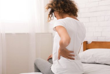 Afrikalı-Amerikalı kadın yatağın üstüne oturan uyku sonra sırt ağrısı olan