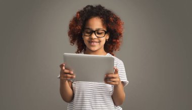 Küçük Afro-Amerikalı kız gri arka planda tablet bilgisayar kullanıyor.