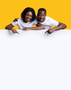 Mutlu Afro-Amerikan çift sarı stüdyo arka planındaki boş reklam panosuna işaret ediyor. Neşeli genç siyah erkek ve kadın reklam ya da metin için boş alan gösteriyor.