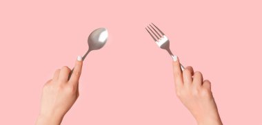 Metal kaşık ve çatalı pembe arka planda tutan kadın ellerini kapat.