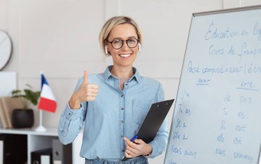 Dost canlısı bayan öğretmen yabancı dil okulunu tavsiye ediyor, başparmak hareketi gösteriyor, Fransızca dersi veriyor. Eğitim hizmetlerinden memnun olan olumlu genç öğretmen