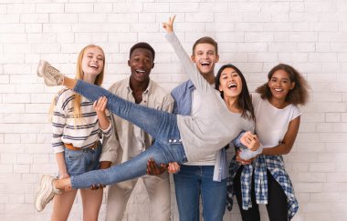 Joyful international group of students lifting asian girl up, having fun over white wall background