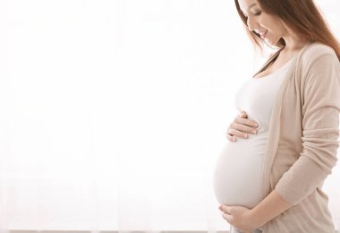 Doğmamış çocukla birlik olmak. Mutlu hamile kadın karnına dokunuyor, beyaz pencere arkası boş.