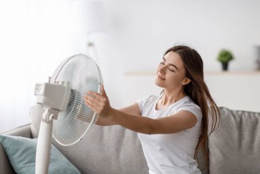 Avrupalı genç bir kadının sıcaktan muzdarip olmasına kanepede oturup soğuk hava almasına, kendine hayran olmasına, oturma odasının içinde serinlemesinin keyfini çıkarmasına sevindim. Yaz havası, evde klima olmadan aşırı ısınma.